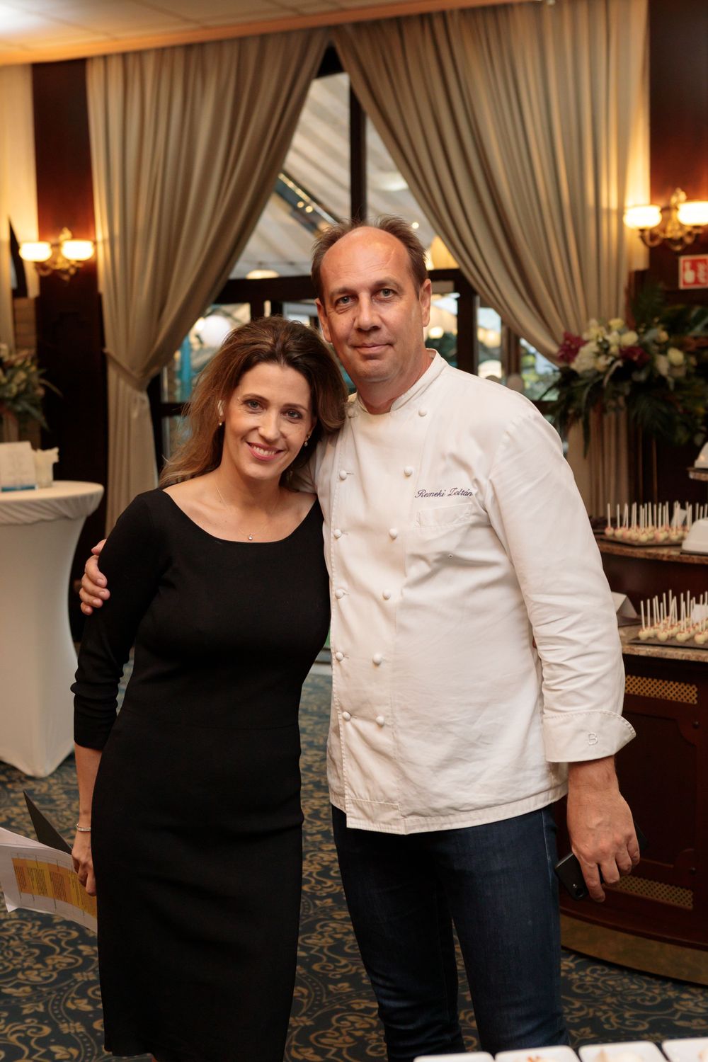 Professional chef in white uniform poses in an elegant restaurant setting.