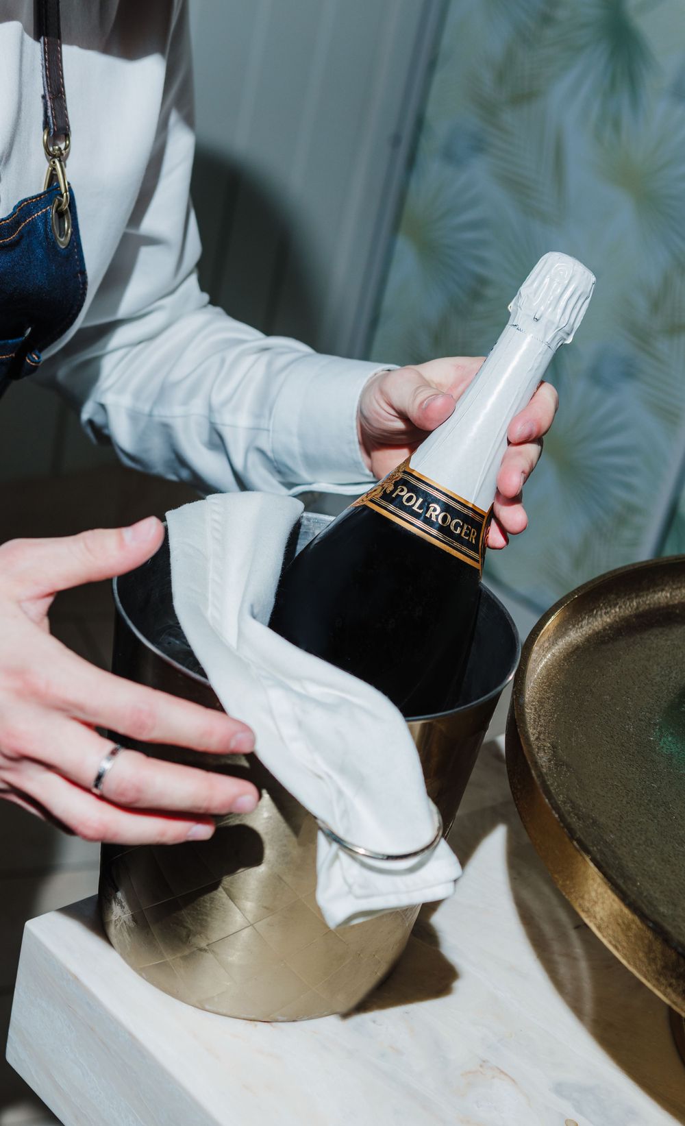 Hands opening champagne bottle wrapped in white cloth.