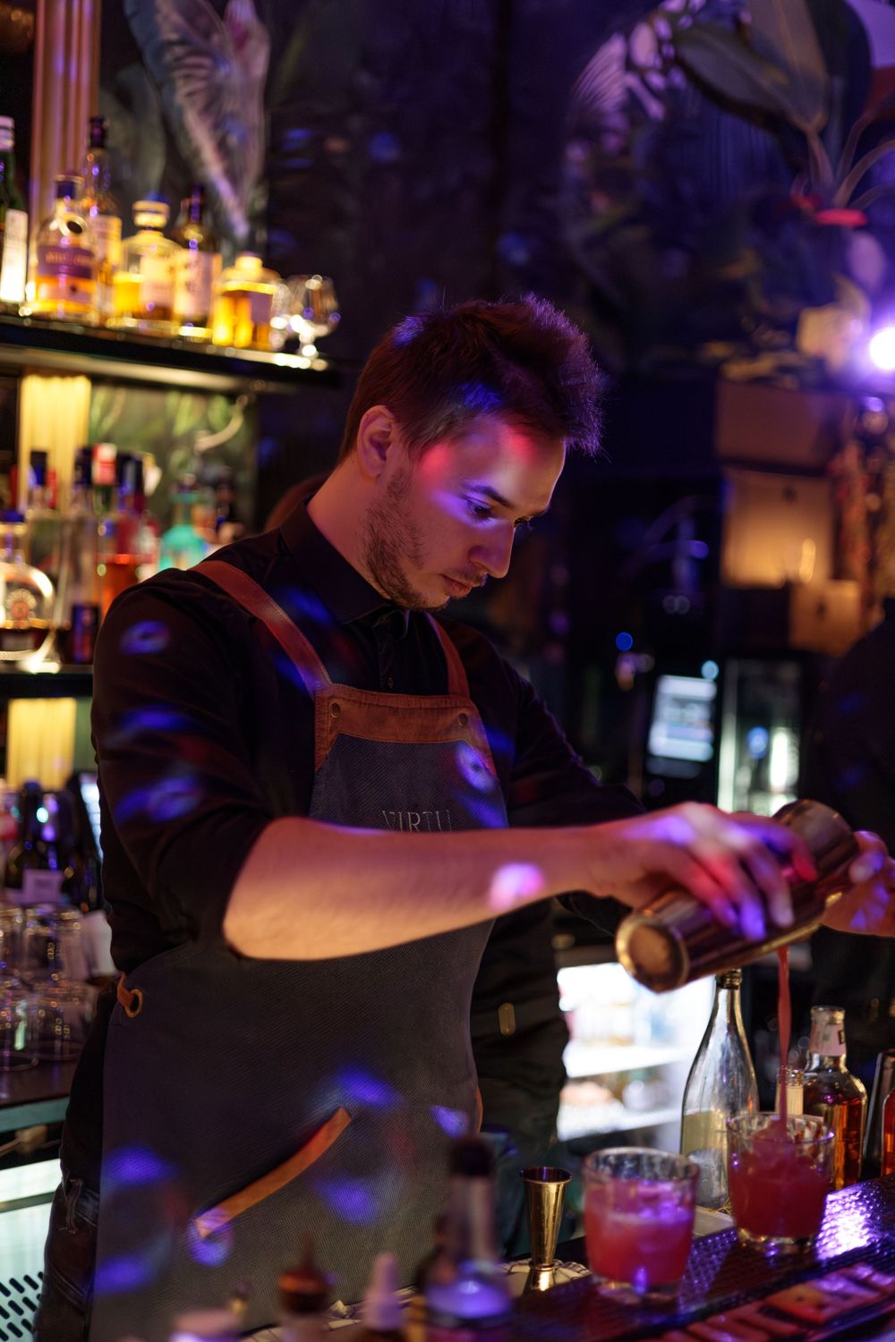 Bartender mixing cocktails in moody lighting at an upscale bar.