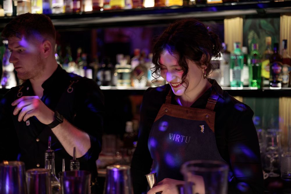 Bartenders working behind a dimly lit bar with purple lighting.