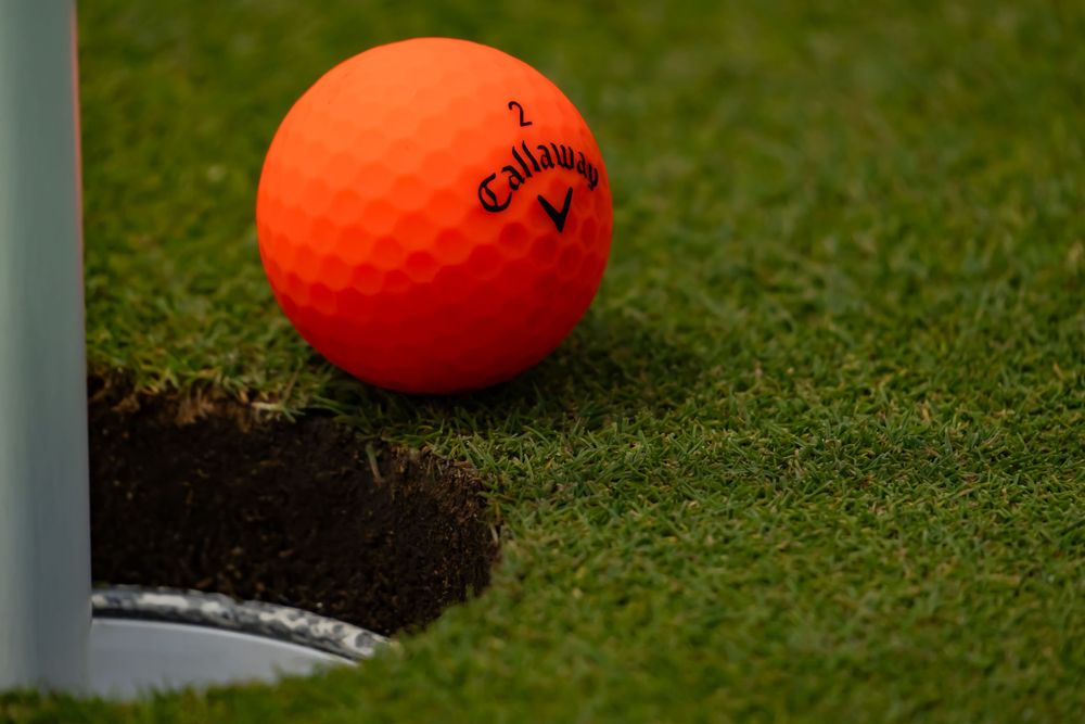 Bright orange golf ball resting near a hole on the green.