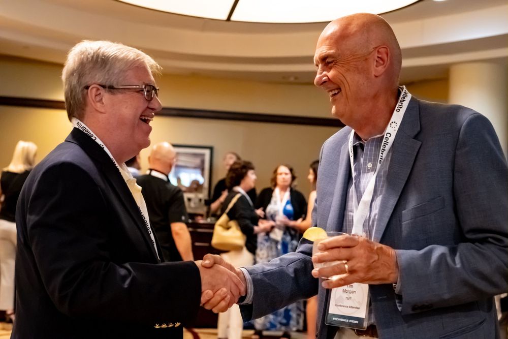 Two business professionals share a handshake and smile during a conference meeting.