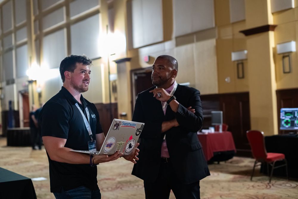 Two professionals having a discussion while one holds a laptop in a conference hall.