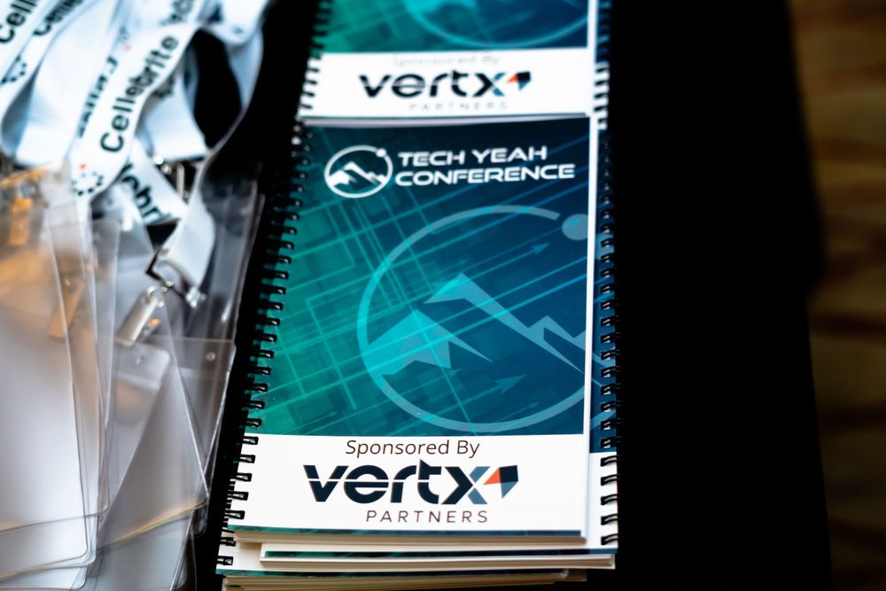 Vertx conference spiral notebook with teal branding displayed on dark surface with glassware.