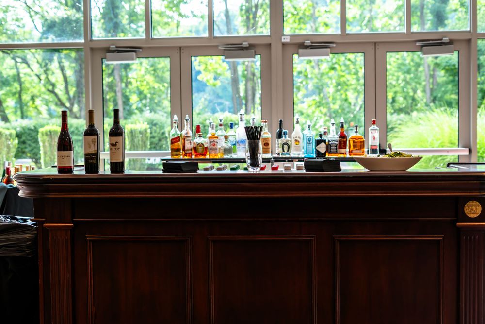 A well-stocked wooden bar displays various bottles of wine and spirits against bright windows.