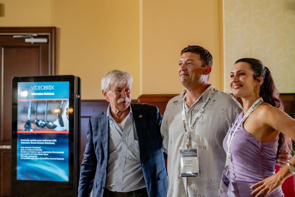 Conference attendees gather near a digital display screen during a networking event.