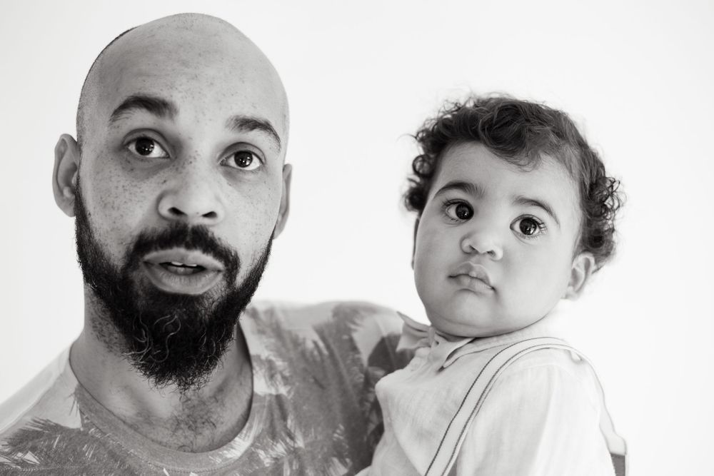 Intimate black and white portrait of parent and child against white backdrop.