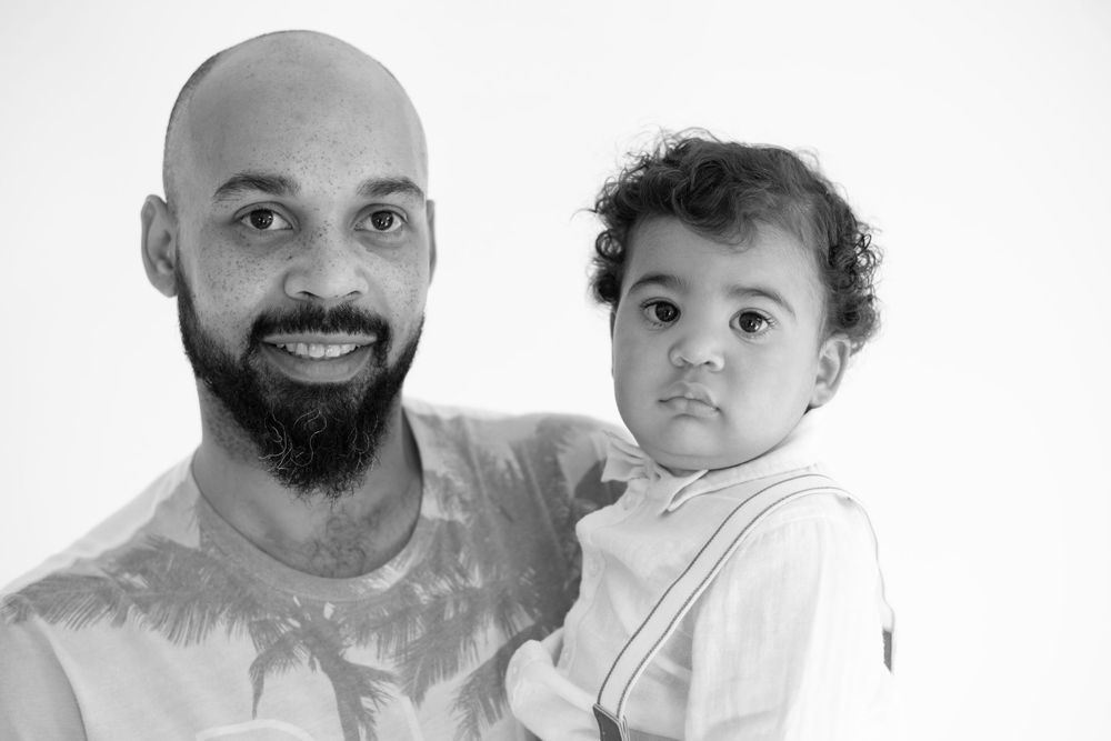 Studio portrait in black and white of parent and child against plain background.
