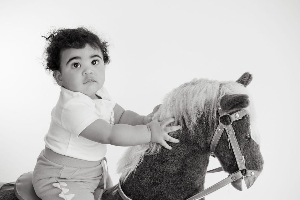 Black and white photo of toddler on rocking horse toy.