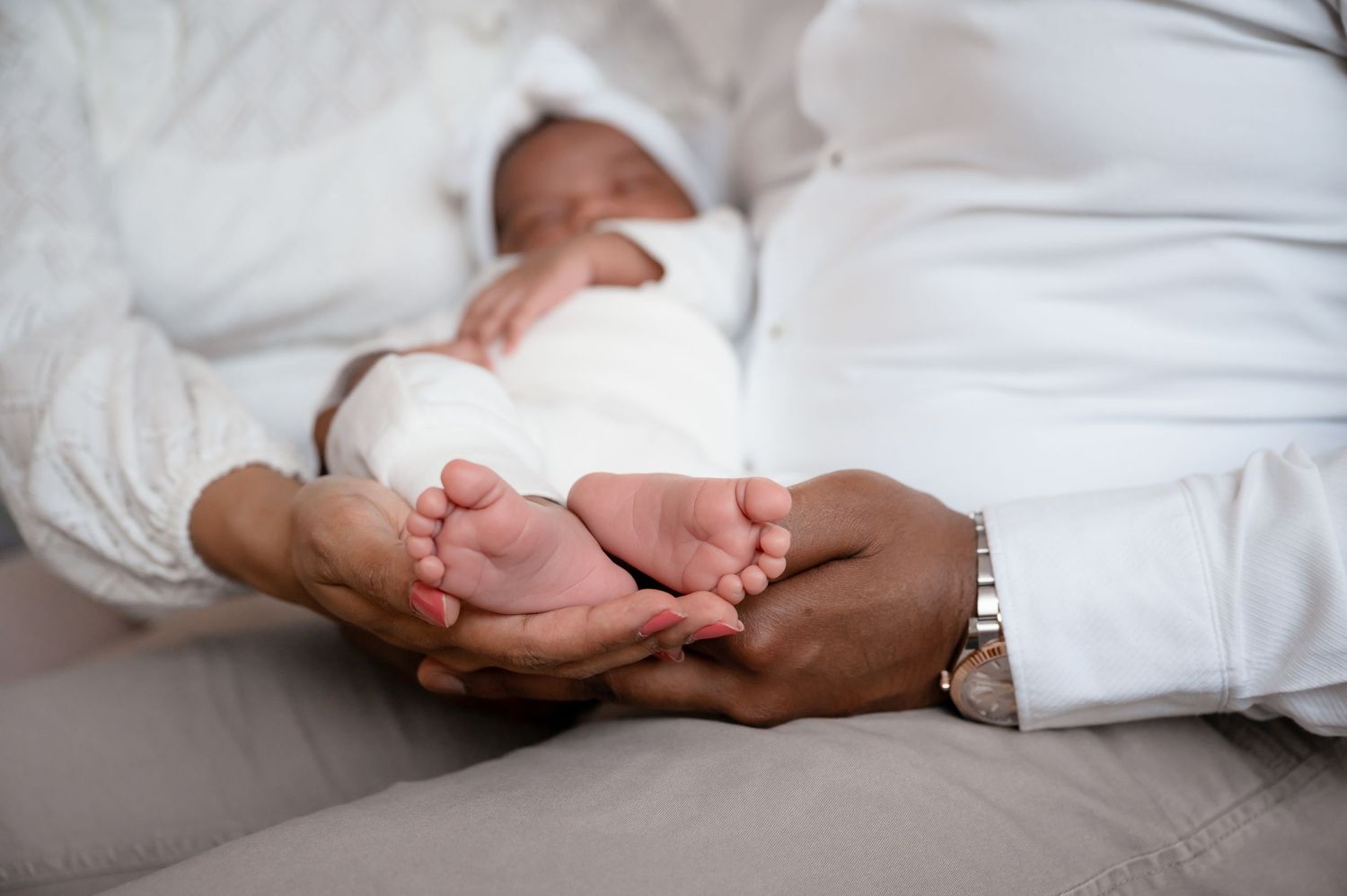 Tender moment showing tiny feet being gently cradled on white bedding.