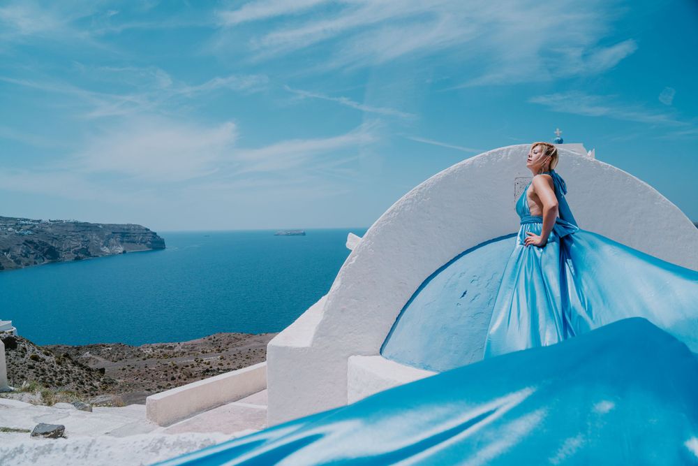 Turquoise dress fabric flowing against white architecture and Mediterranean views.