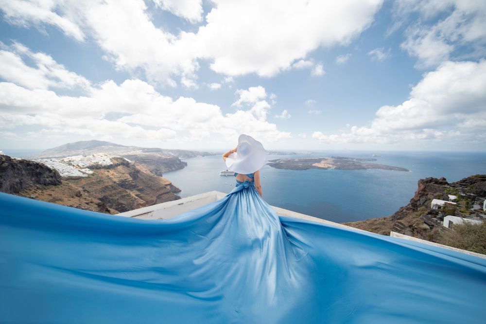 Blue dress fabric creates dramatic silhouette against Santorini caldera view.