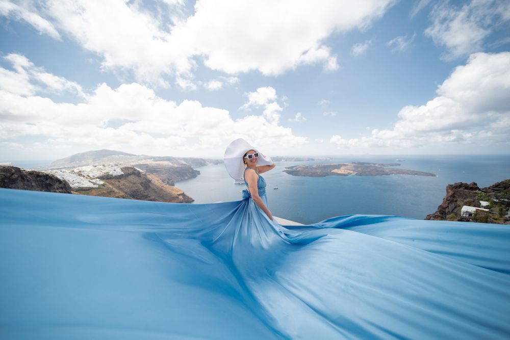 Aerial view of flowing blue gown creating dramatic waves against Mediterranean coastline.