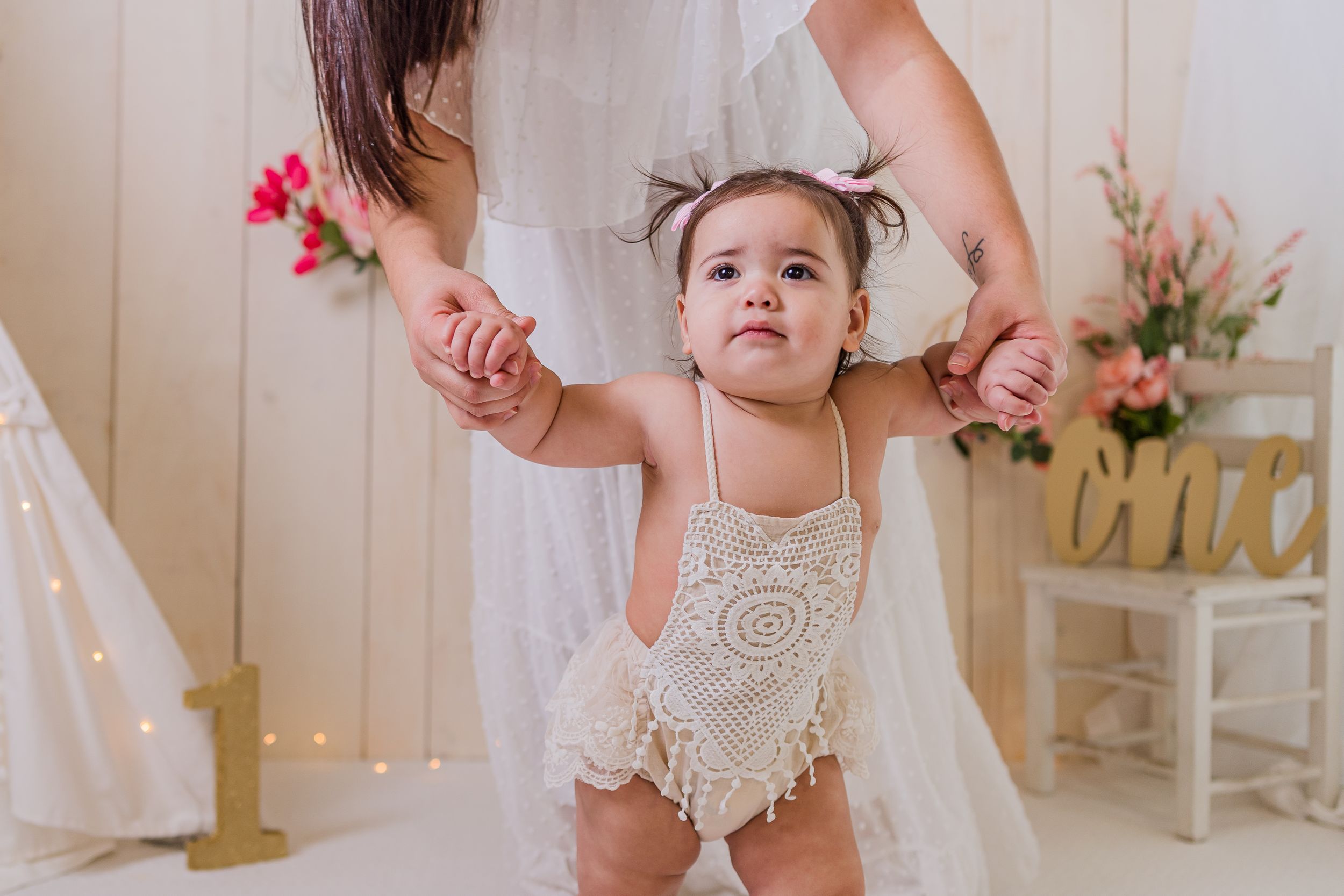 Small child in white lace romper being held up while dancing in a pink and white decorated room.