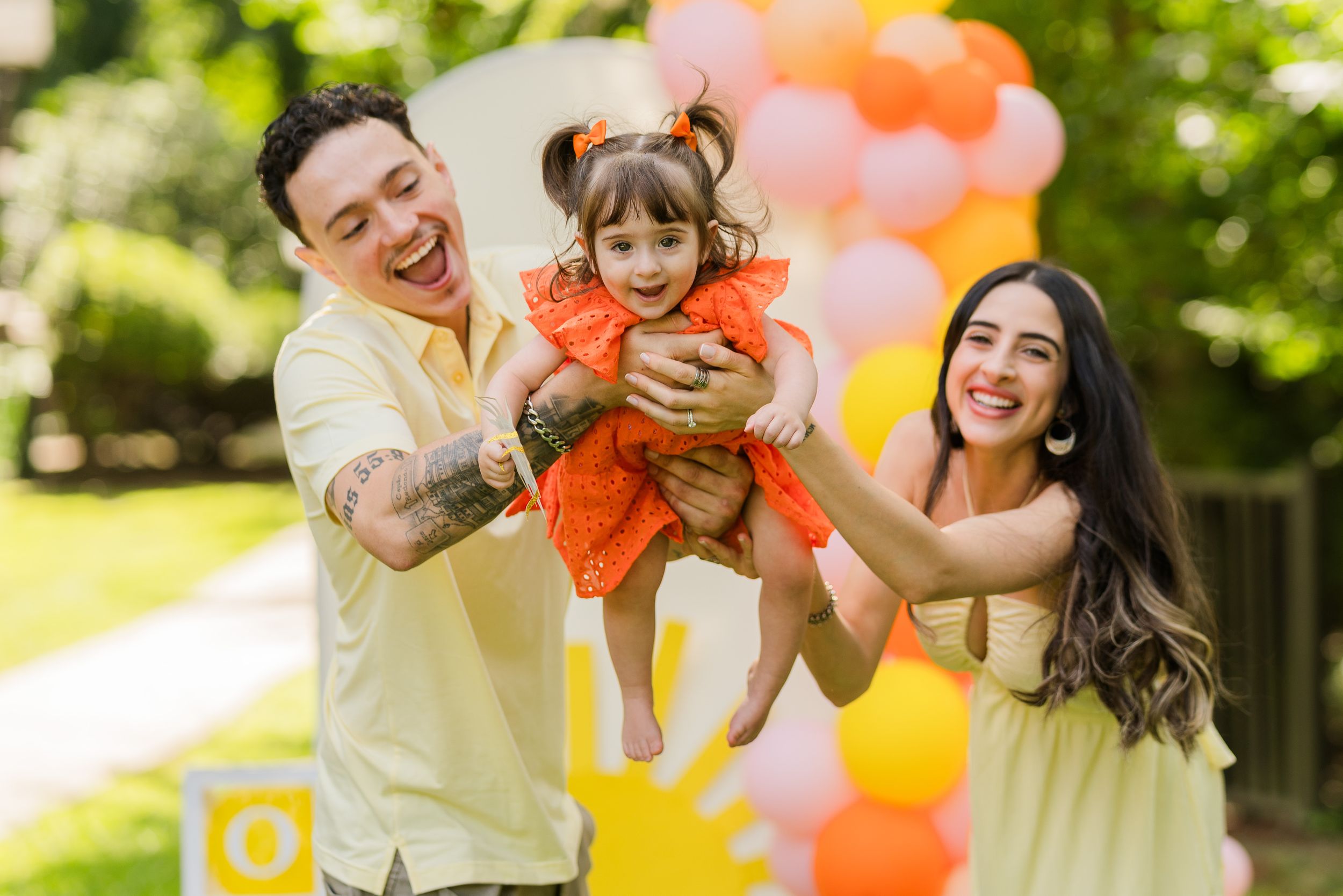 A couple in a park setting with colorful orange and pink balloons creates a joyful outdoor scene.