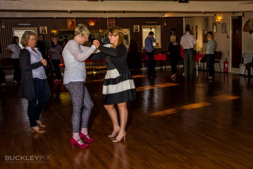 People dancing in a dimly lit indoor venue with wooden floors and walls.