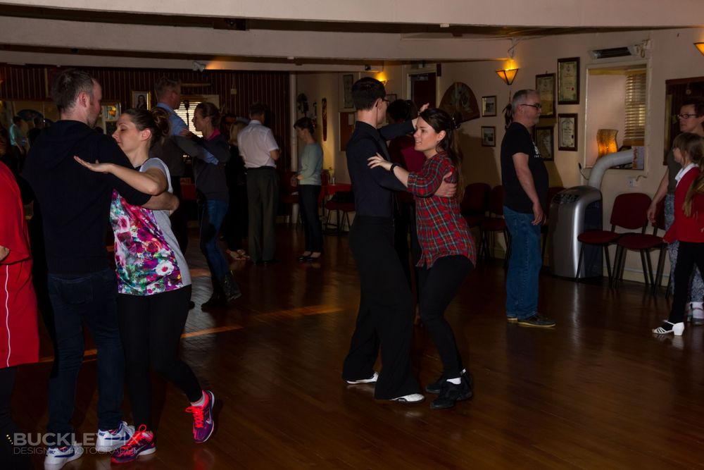 Couples dancing together on wooden floor in indoor social gathering space.
