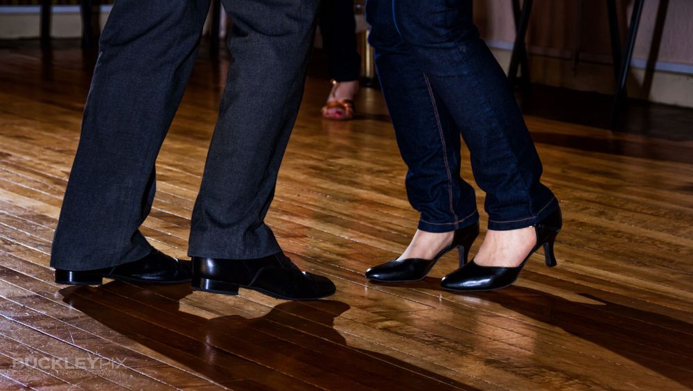 Close-up of dancers' feet in formal shoes on polished wooden dance floor.