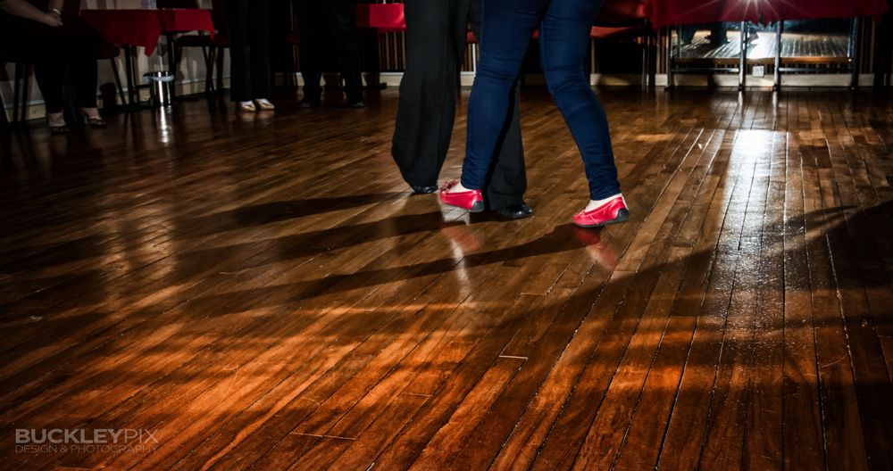 Dancers move across a polished hardwood floor in a spacious dance studio.