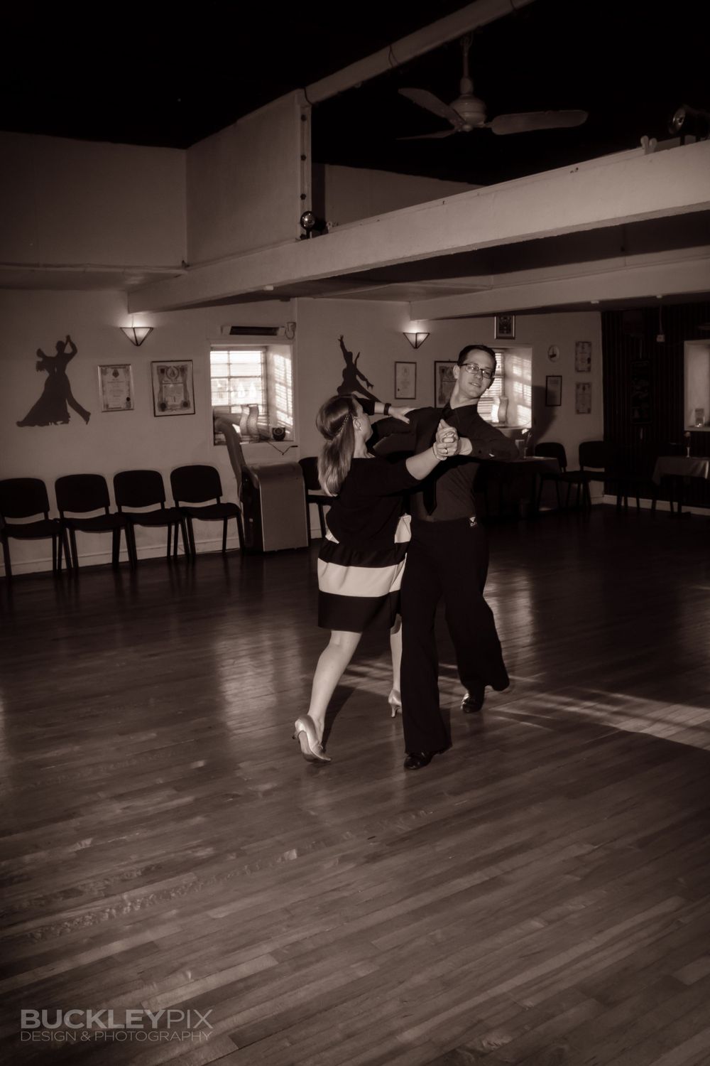 Black and white panorama of dancers practicing in a mirrored studio space.
