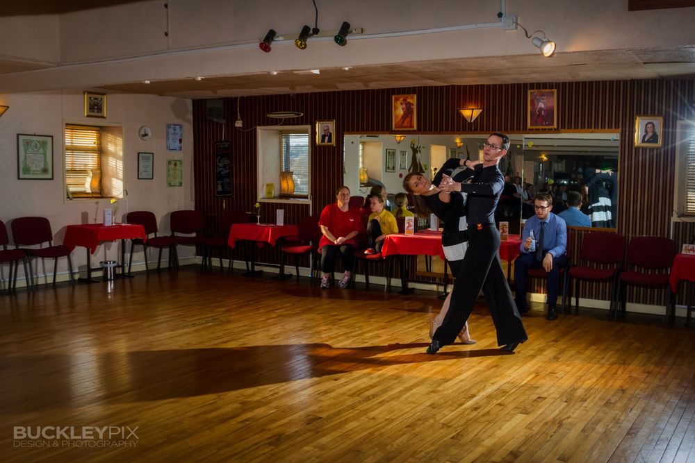 Wide panoramic shot of a dance studio with warm lighting and wooden floors.