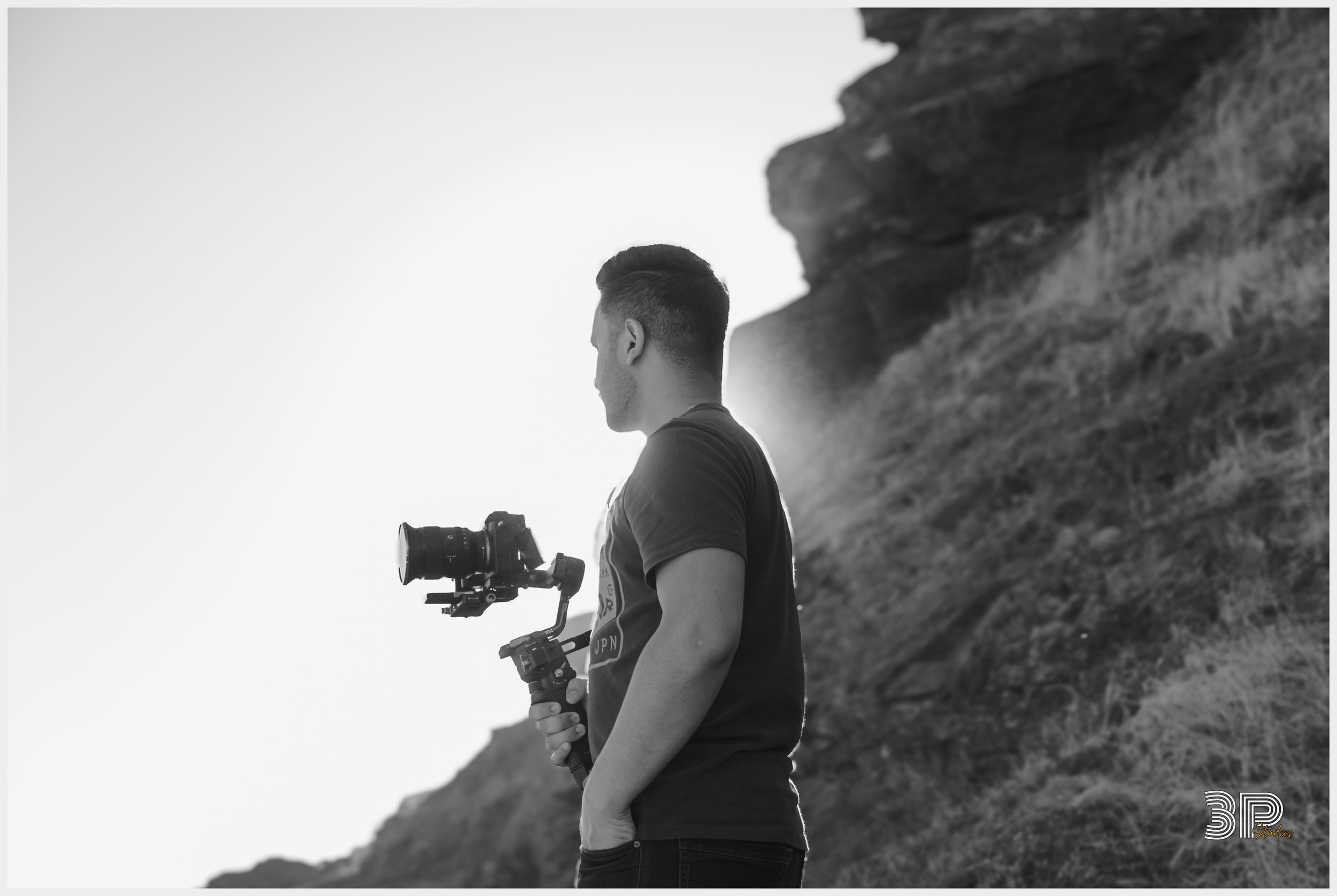 A black and white photo of someone holding camera equipment on a hillside.