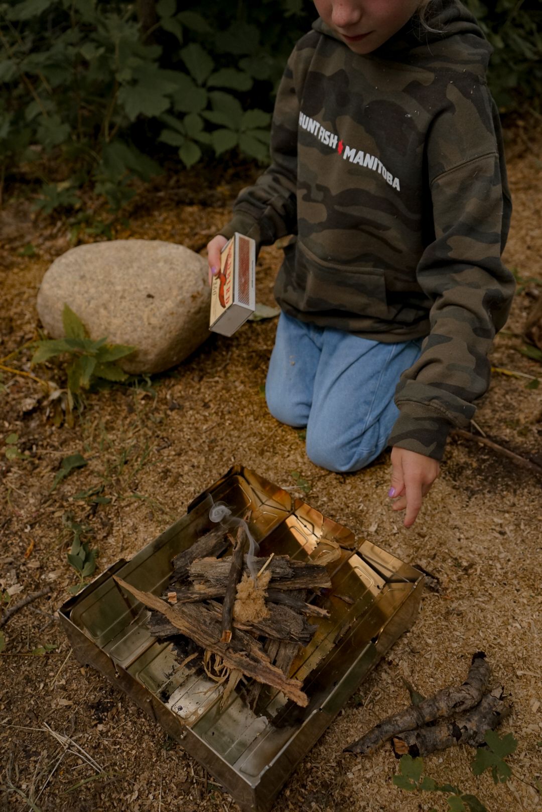 Setting up kindling and firewood in a portable camping stove outdoors.