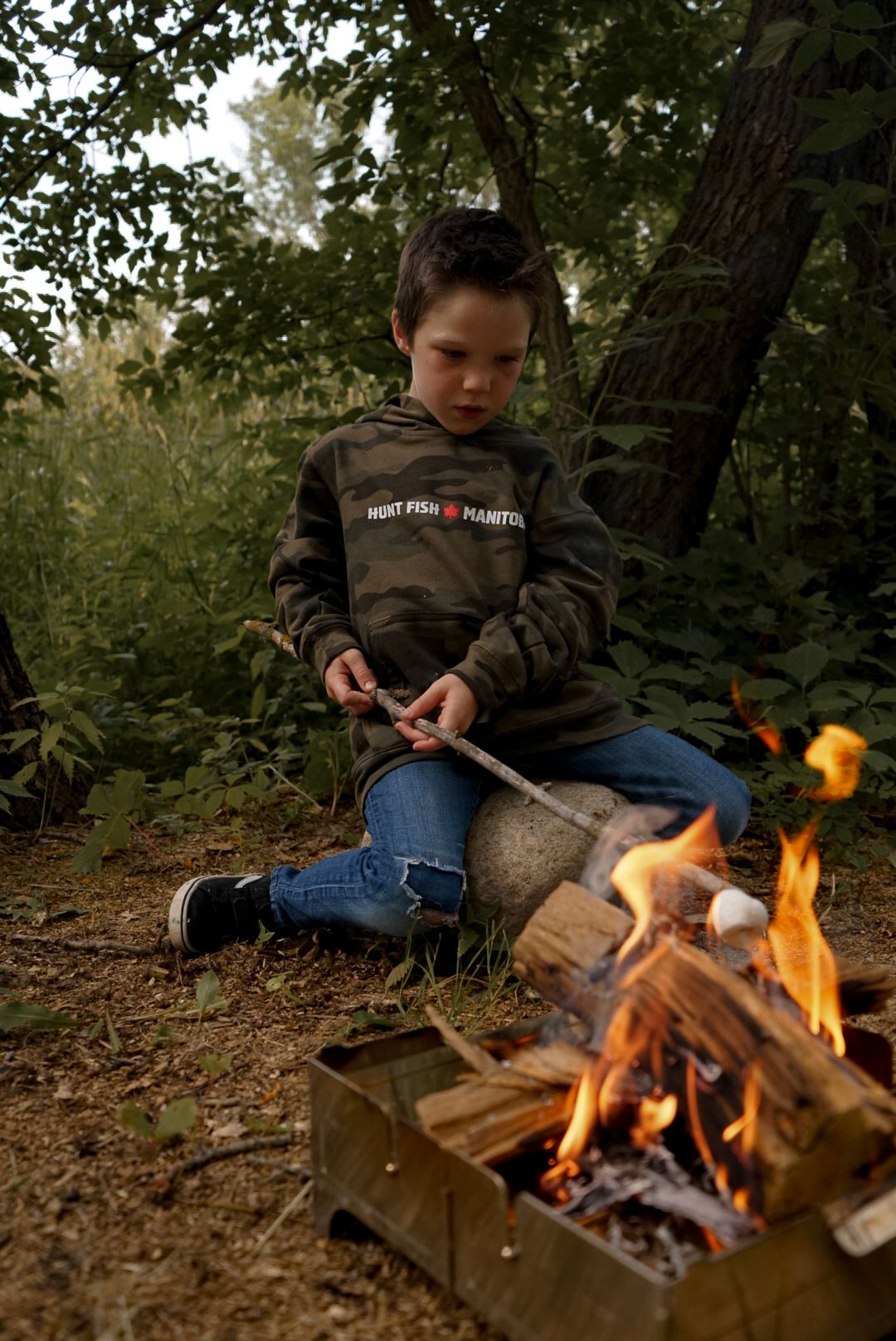 Portable camping stove with flames burning wood in an outdoor forest setting.