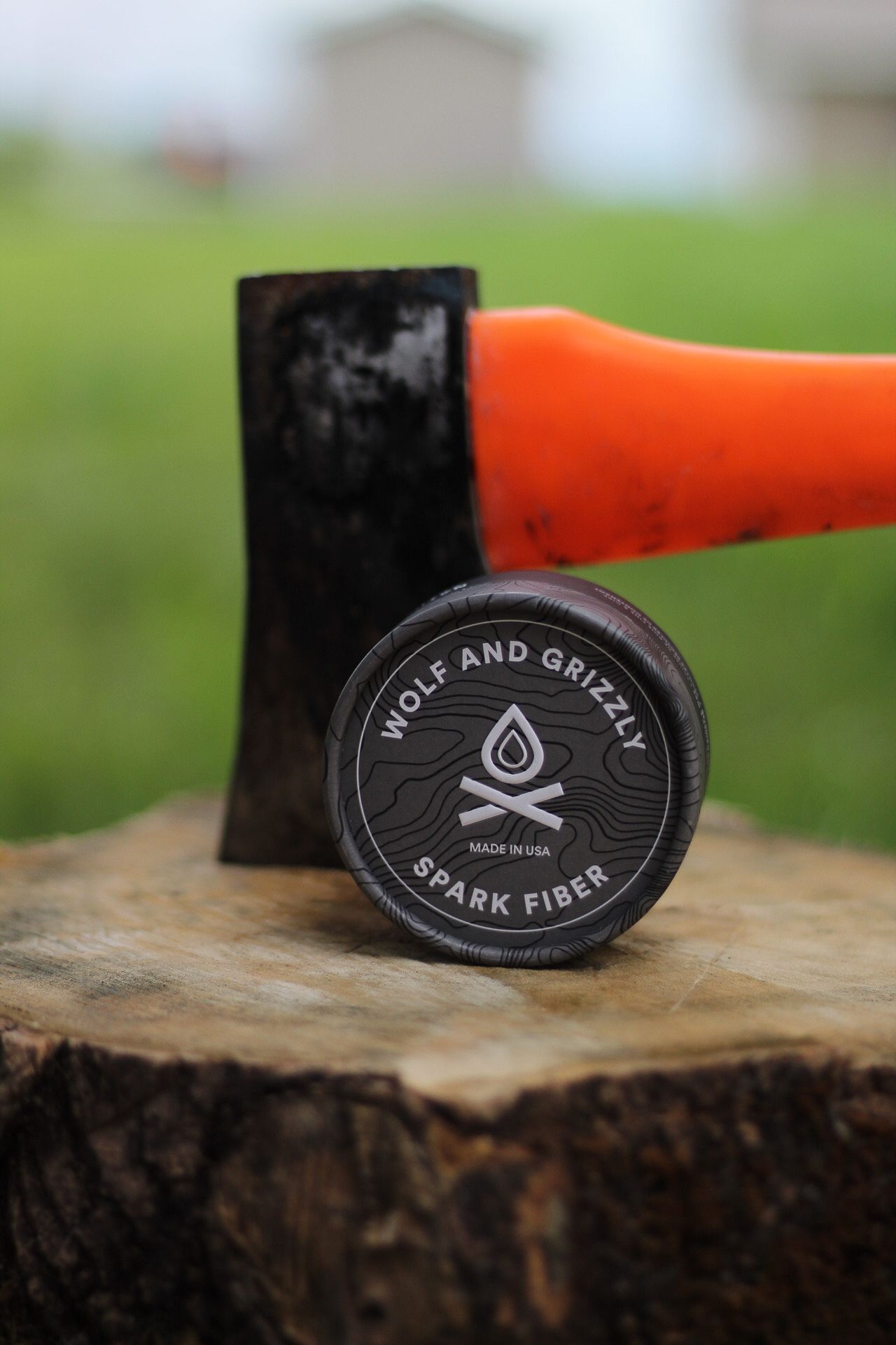 Wolf and Grizzly brand logo patch displayed on wooden stump with orange tool in background.