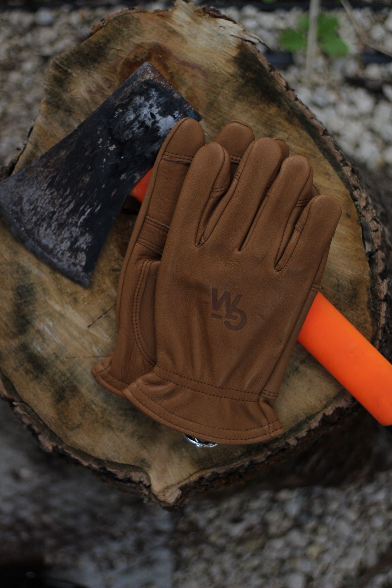 Brown leather work glove with axe on wooden chopping block.
