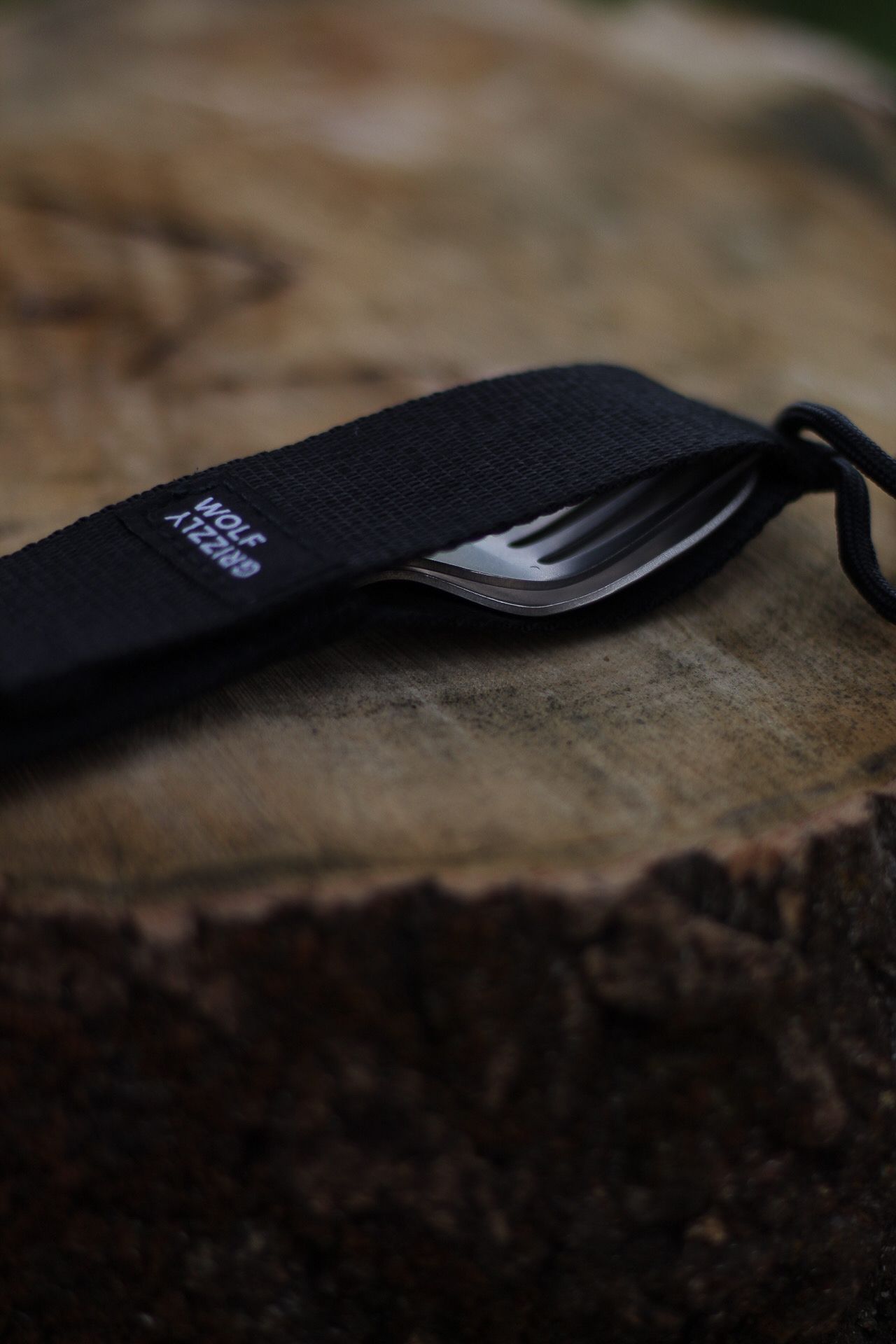 Black utensil holder pouch with fork on rustic wooden surface.