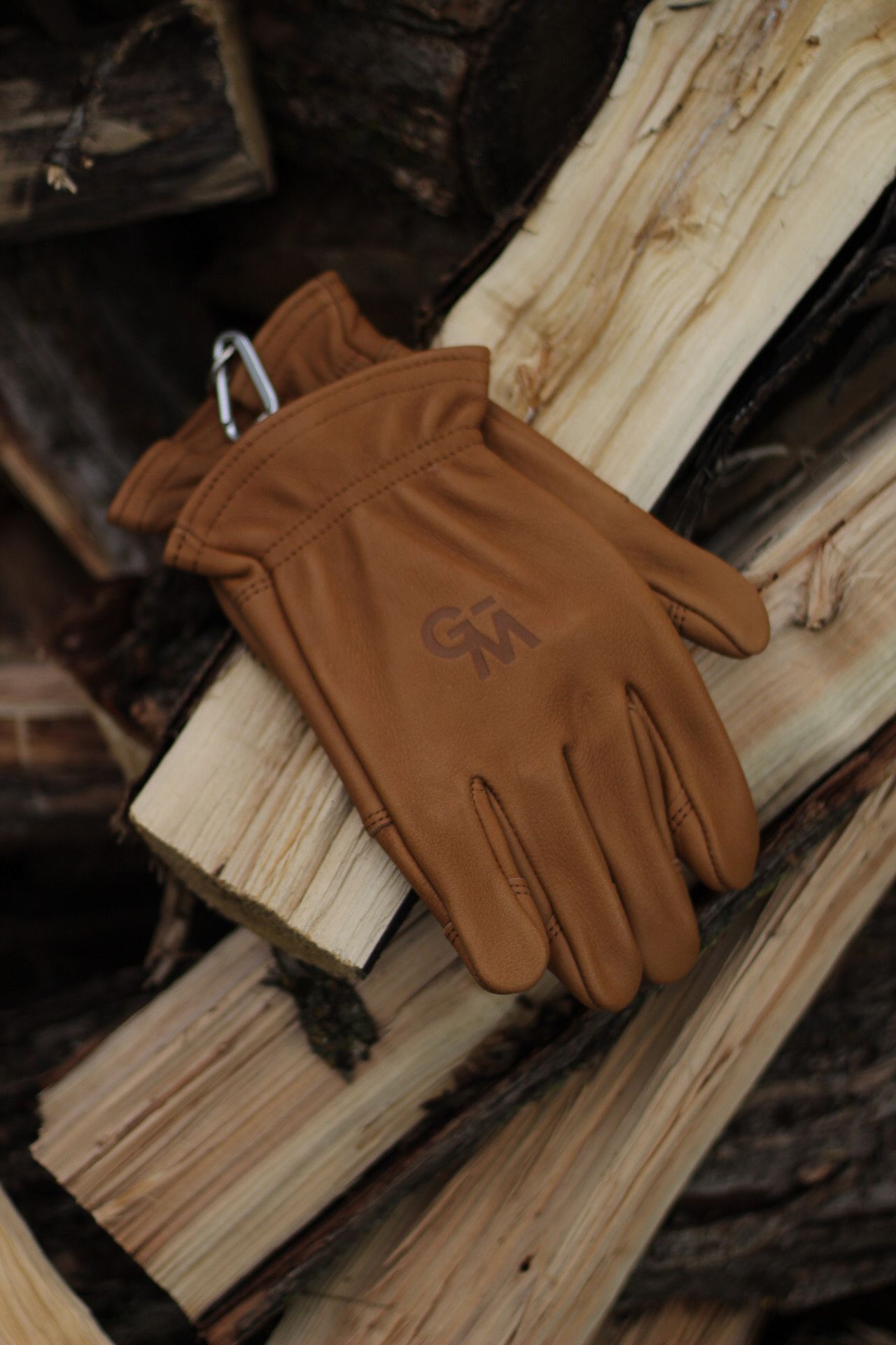 Brown leather work gloves laid out on split firewood logs.