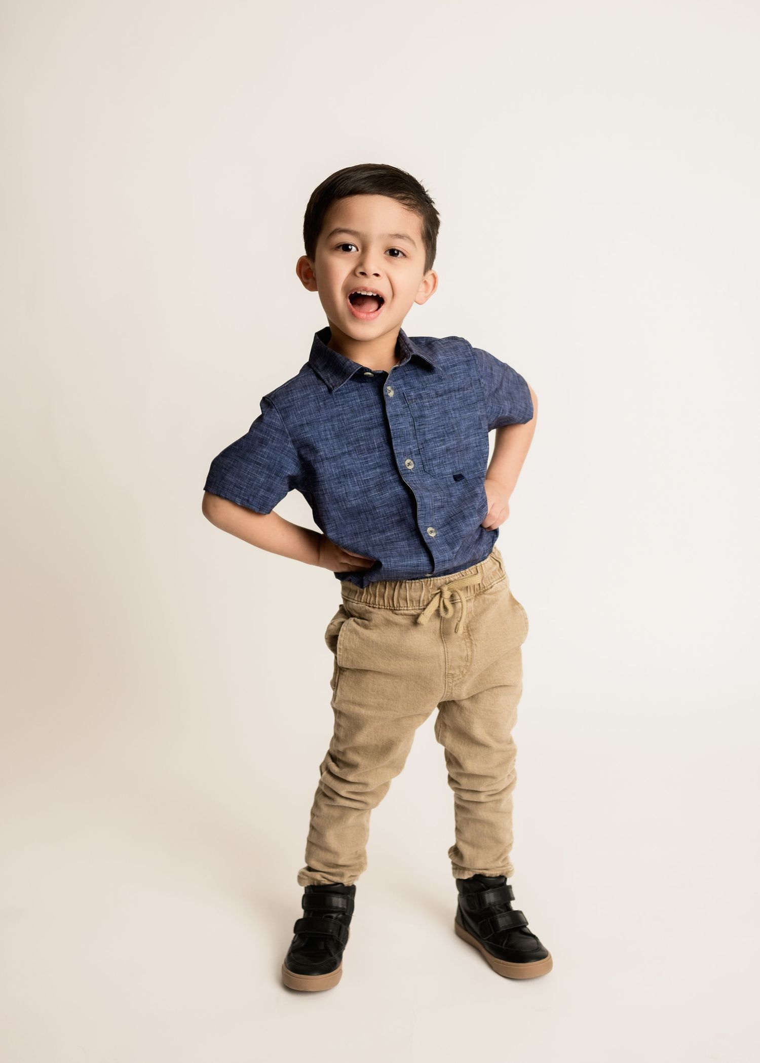 Energetic young boy posing with hands on hips mouth open in fun studio birthday portrait photo.