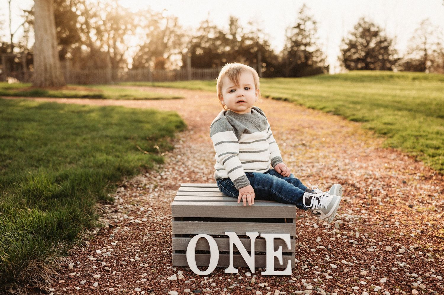 Adorable one year old baby sitting on wooden crate with ONE sign on a scenic outdoor path.