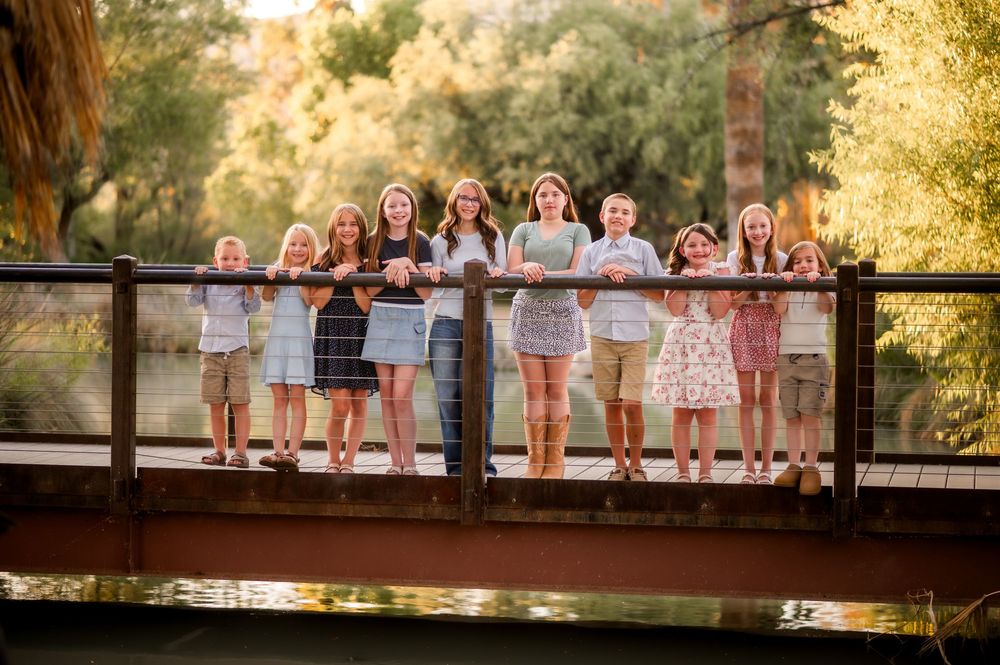 Group of children posing on a wooden bridge surrounded by lush green trees in warm golden light.
