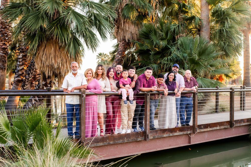 Extended family smiling together on a bridge with palm trees and a calm pond backdrop.