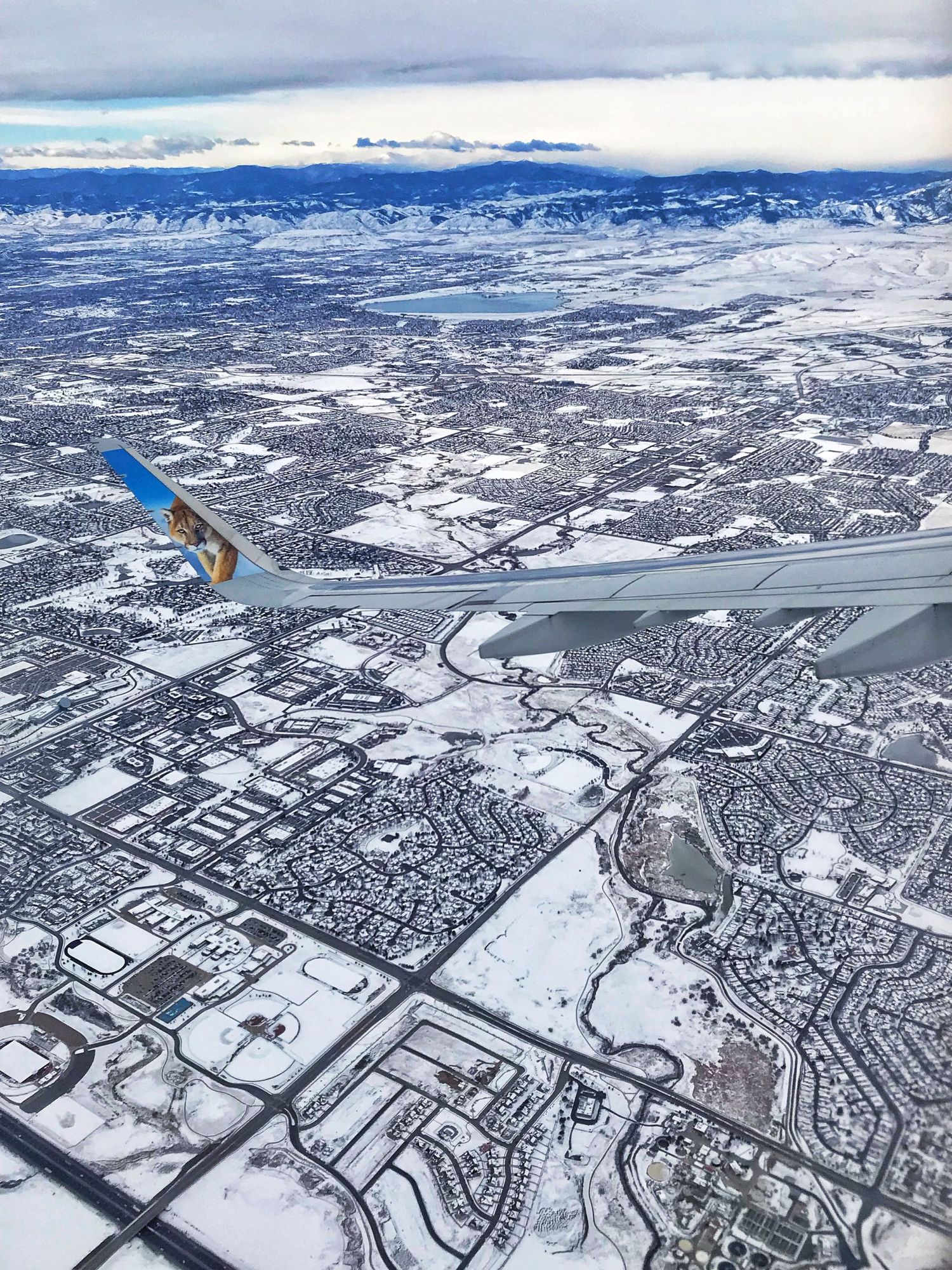 Aerial view of a snow-covered city with an airplane wing visible over residential areas.