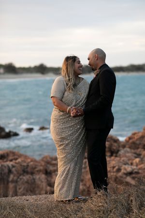 A couple shares an intimate moment on rocky coastal cliffs at sunset with turquoise ocean waters in the background.
