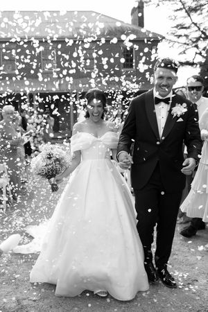 Black and white photo of a joyful bride and groom walking through confetti after their wedding ceremony.