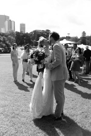 Black and white photo of a bride and groom sharing their first kiss outdoors at a wedding ceremony.