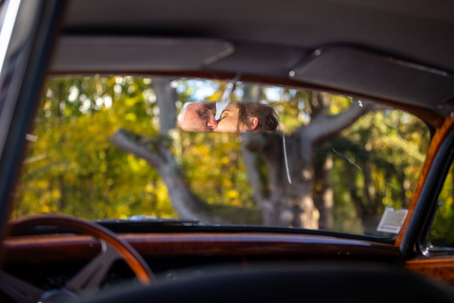 View through vintage car window showing autumn trees and natural scenery.