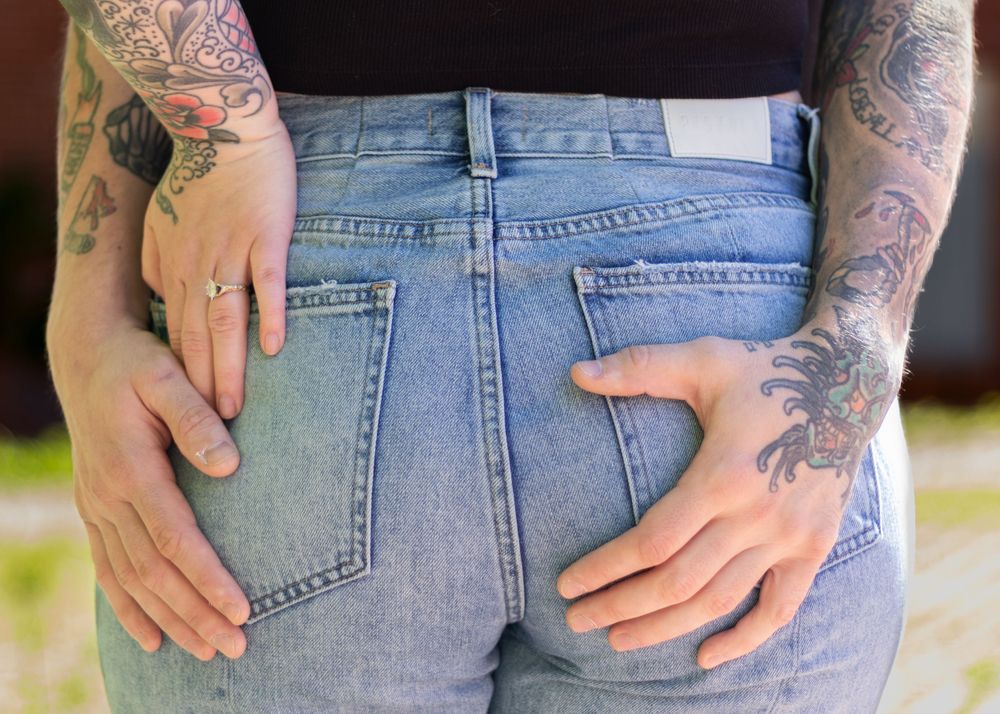Back view of tattooed person wearing blue jeans showing arm artwork.