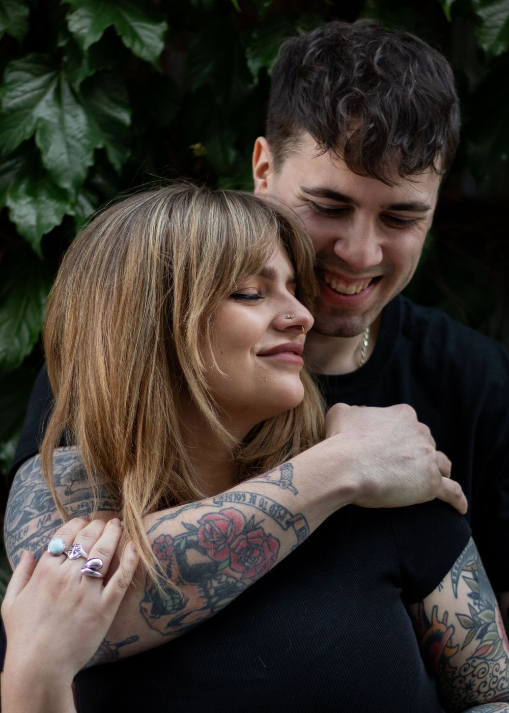 Intimate couple portrait with visible tattoos against leafy background.