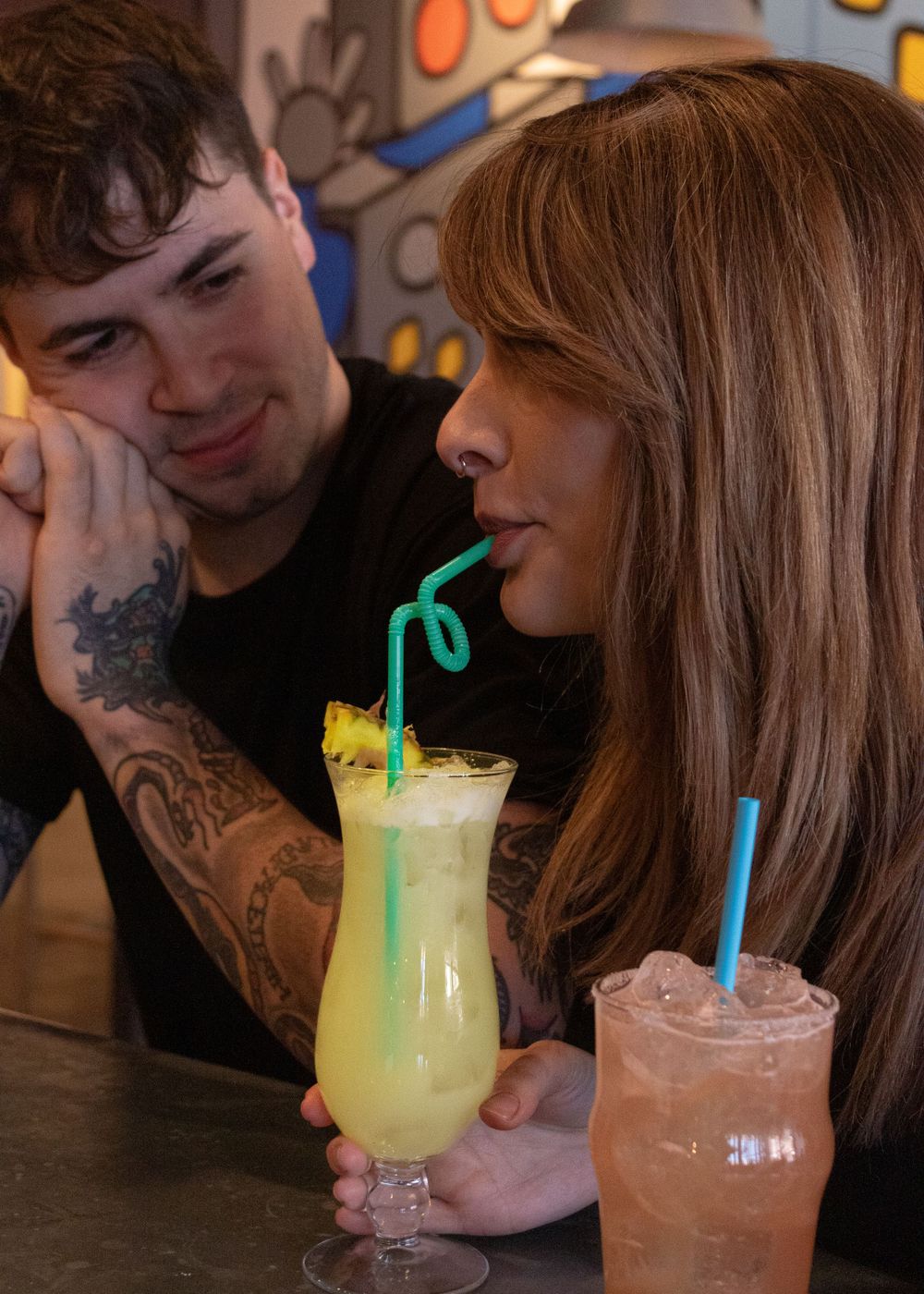Couple at bar with tropical cocktails in stemmed glasses.