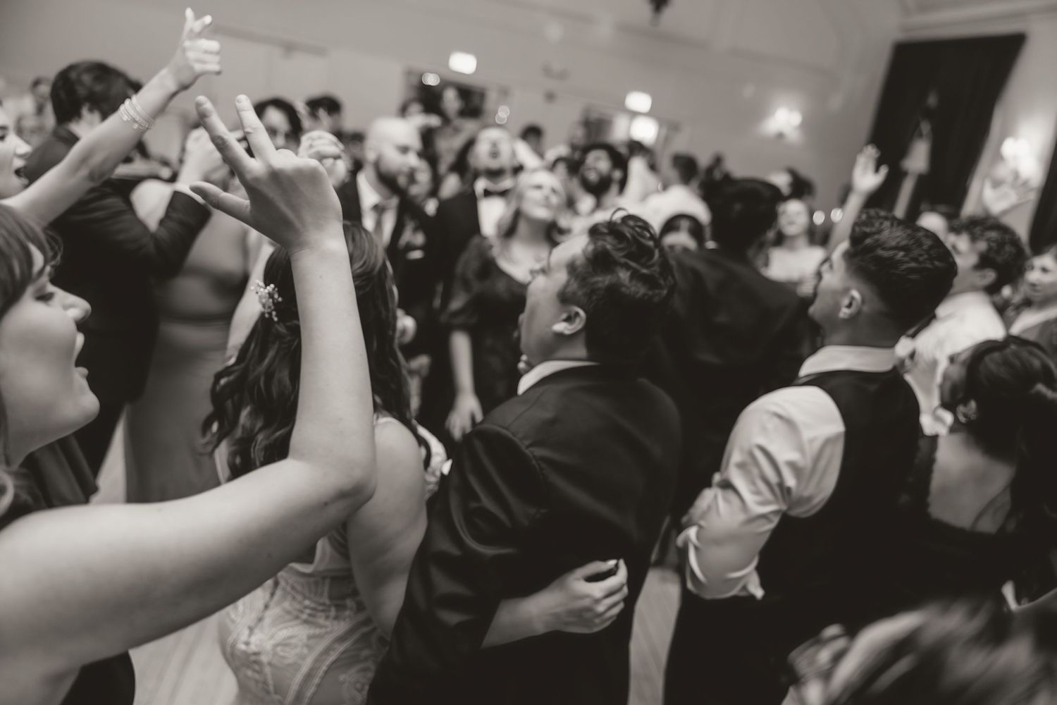 Black and white photo of wedding reception dance floor celebration with raised hands.