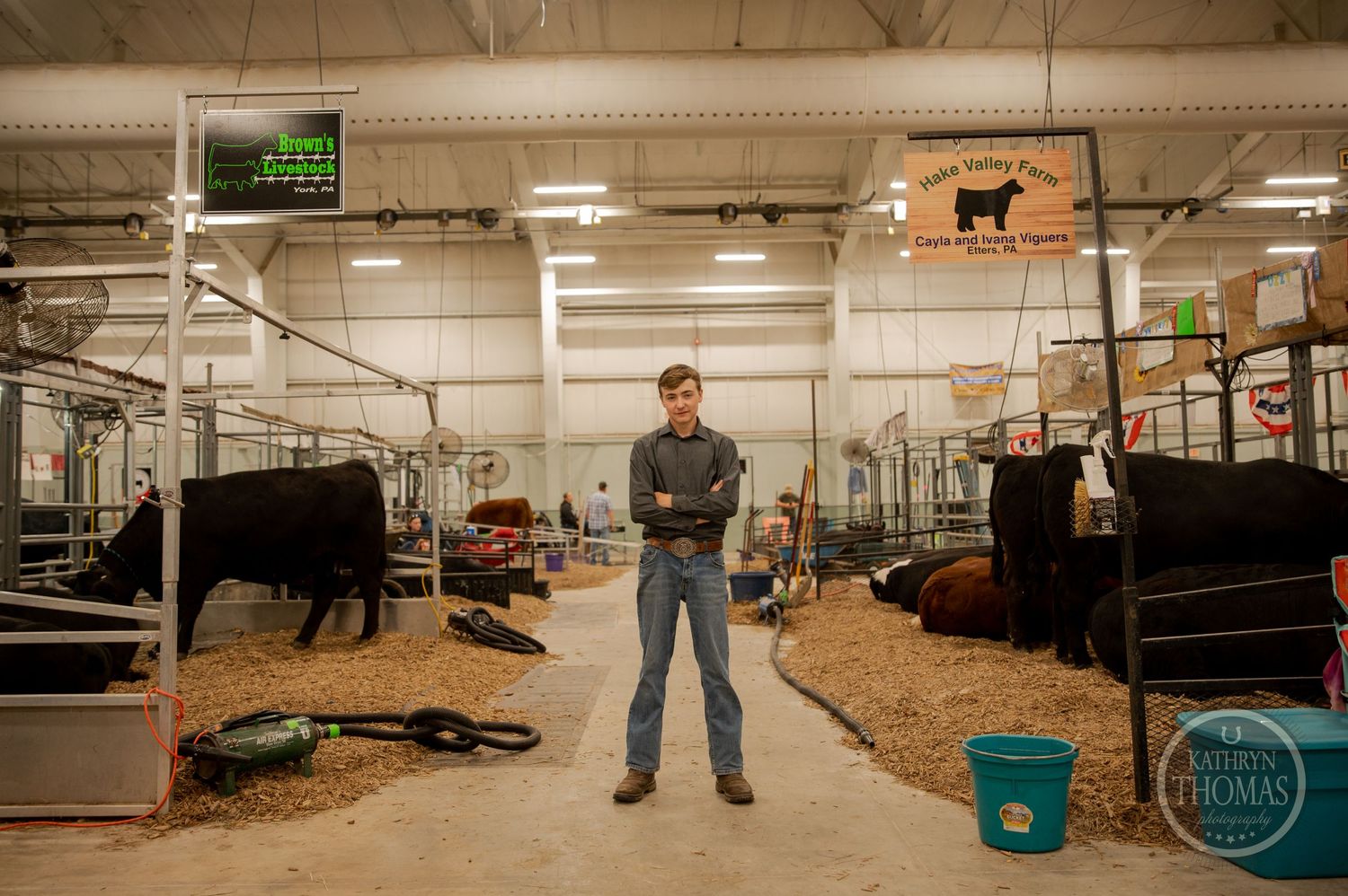 A person stands in a livestock barn with industrial lighting and bedded stalls.