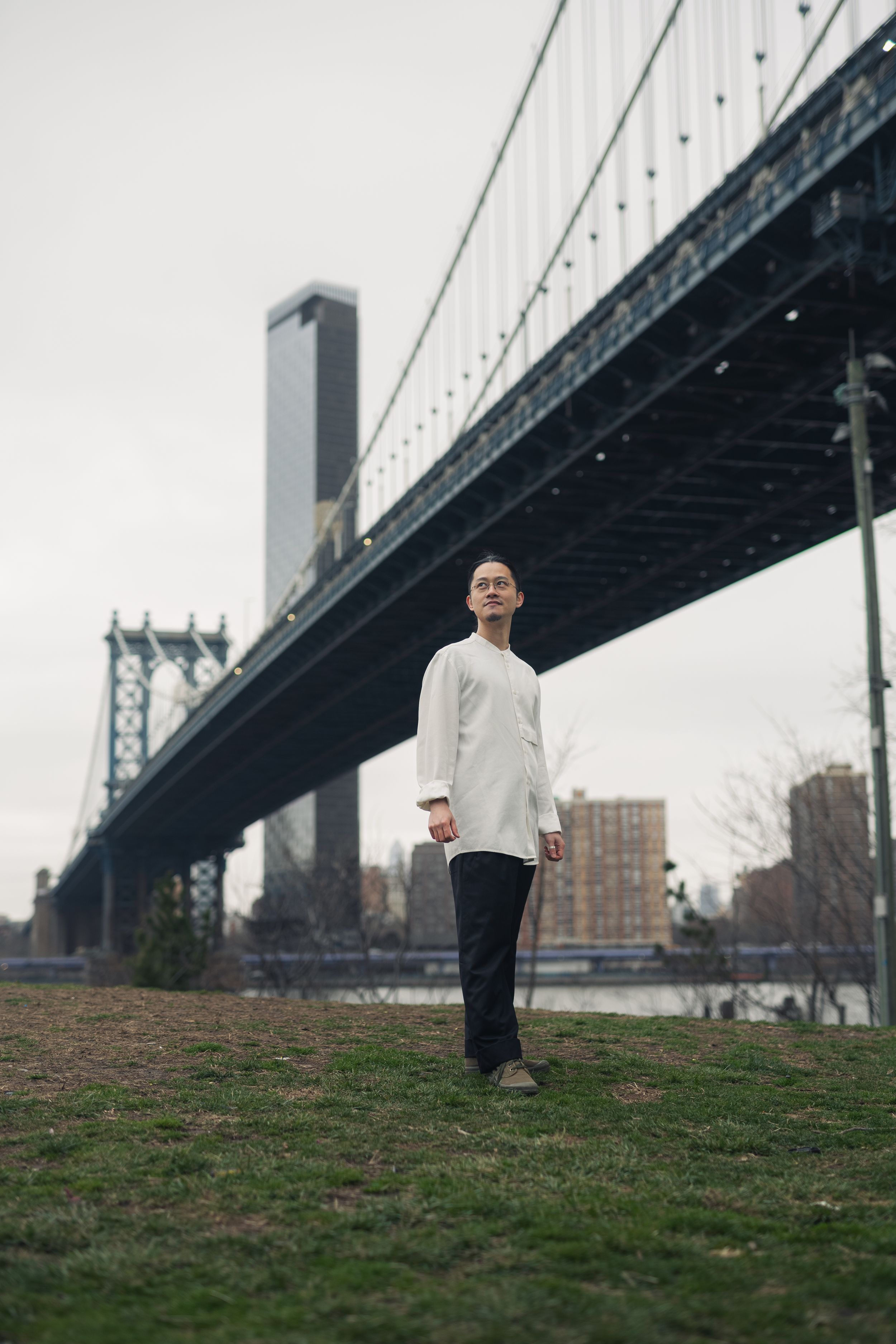 Person in black and white outfit standing on grassy hill beneath a large bridge structure.
