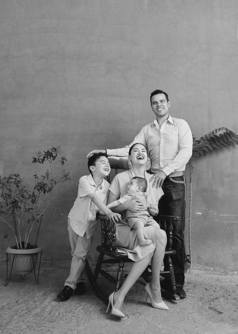 A family shares a joyful moment together while posing for a black and white portrait against a simple backdrop.