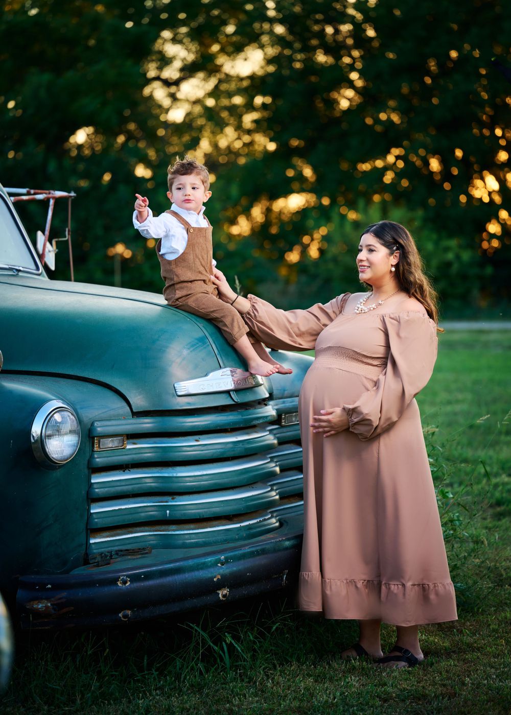 A maternity photo featuring a classic turquoise vintage truck and a brown dress in golden sunset lighting.
