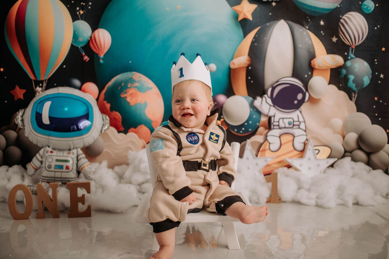 Space themed first birthday setup with astronaut decorations and cloud-like backdrop.